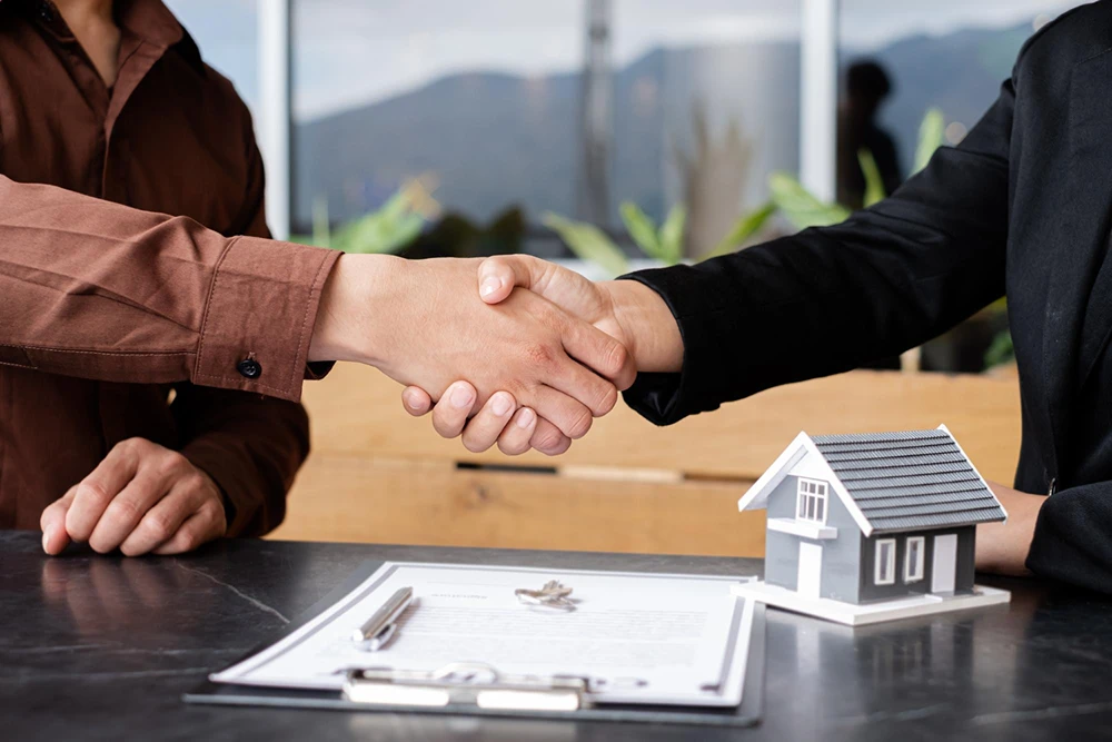 Two people shaking hands over house model and contract deal