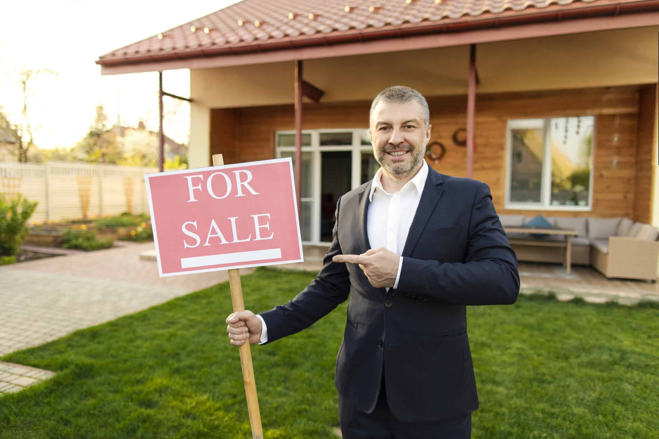 Smiling real estate agent holding a for sale sign in front of house