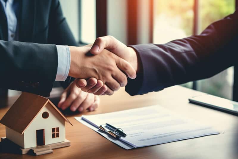 Handshake over house model and contract on office desk