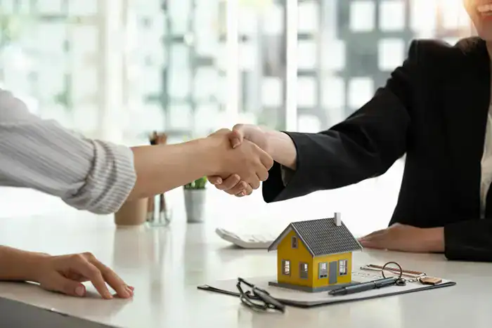 Handshake over yellow house model keys and contract on desk